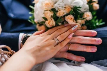 Руки наречених тримають букет рожевих троянд на весіллі.