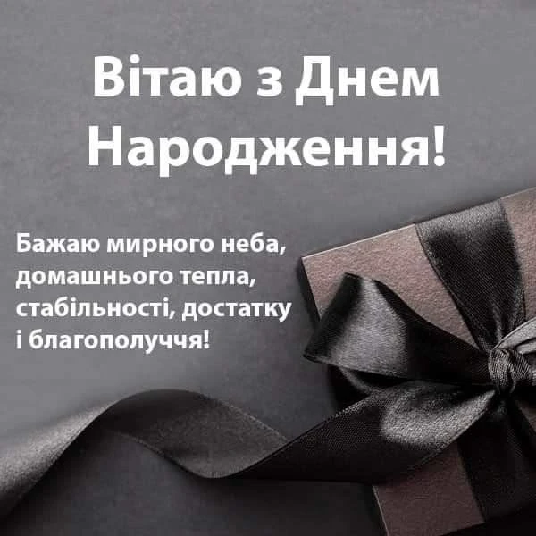 Чорна подарункова коробка з чорною стрічкою на сірому фоні.