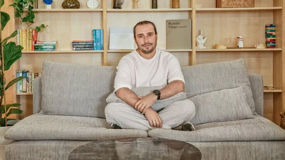 Чоловік сидить на дивані в інтер'єрі з полицями та рослинами.